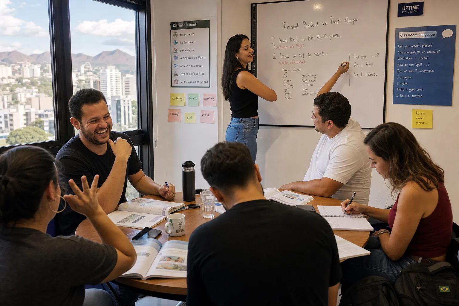 Turma pequena de inglês em escola de Belo Horizonte: professora explicando Present Perfect no quadro, alunos adultos com livros, vista do Buritis pela janela